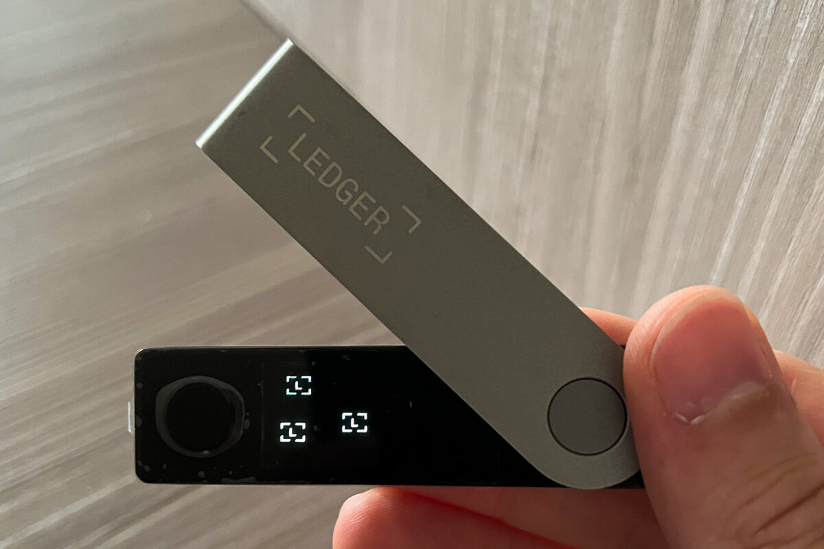 A hand holding a Ledger Nano X hardware wallet with its cover swiveled open